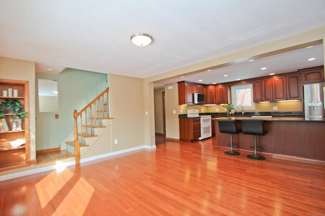 kitchen featuring baseboards, light wood finished floors, appliances with stainless steel finishes, dark countertops, and a kitchen breakfast bar