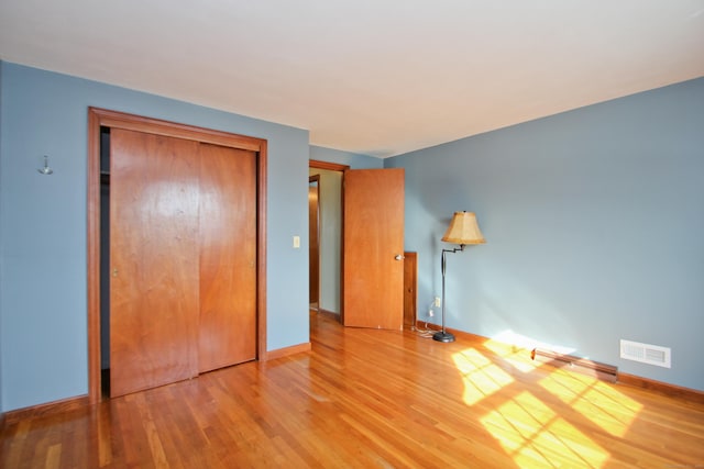 unfurnished bedroom featuring a closet, visible vents, baseboards, and wood finished floors