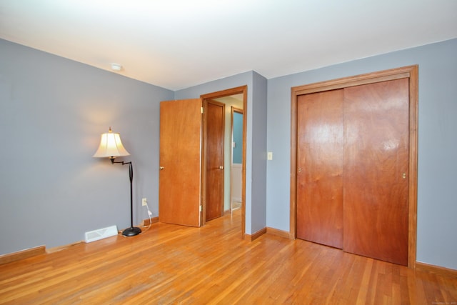 unfurnished bedroom with a closet, visible vents, baseboards, and wood finished floors