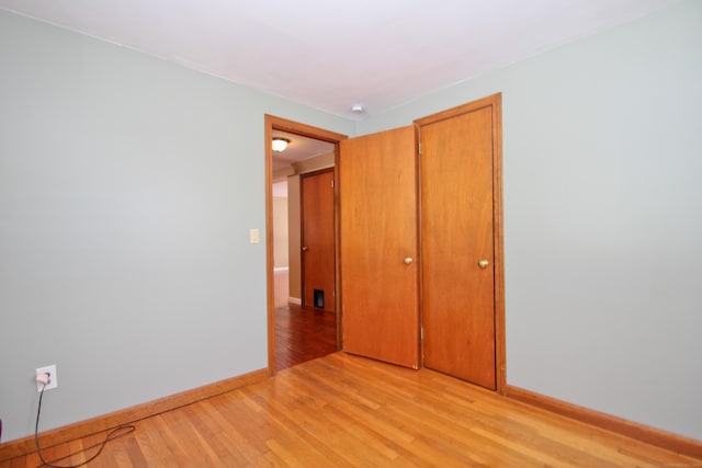 unfurnished bedroom featuring light wood-style floors, baseboards, and a closet