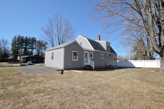 view of home's exterior featuring fence, a yard, a gambrel roof, a chimney, and entry steps