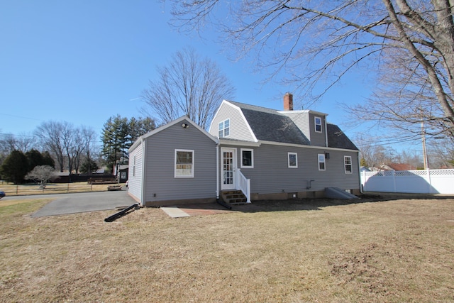 rear view of house with a gambrel roof, a lawn, entry steps, fence, and roof with shingles