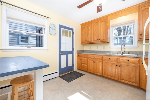 kitchen featuring a breakfast bar, a baseboard radiator, a ceiling fan, brown cabinetry, and a sink