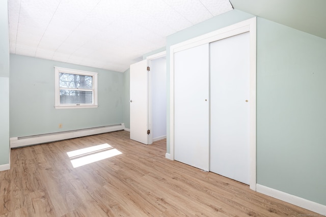 unfurnished bedroom with lofted ceiling, a closet, a baseboard heating unit, and wood finished floors