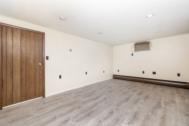 unfurnished room with recessed lighting, a baseboard heating unit, light wood-type flooring, a wall mounted air conditioner, and baseboards