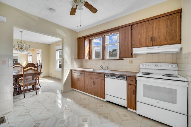 kitchen with under cabinet range hood, white appliances, a sink, decorative backsplash, and brown cabinets