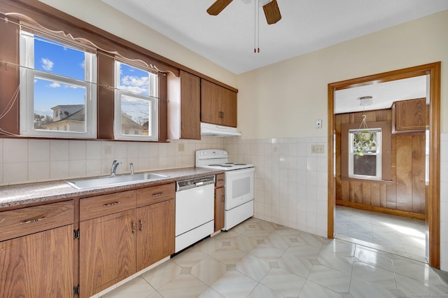 kitchen featuring white appliances, brown cabinetry, light countertops, under cabinet range hood, and a sink