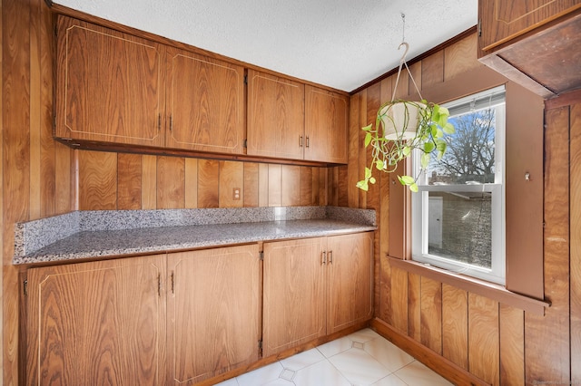 kitchen with wood walls, light stone counters, brown cabinetry, and a textured ceiling