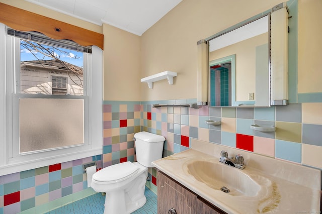 bathroom featuring toilet, a wainscoted wall, vanity, tile walls, and tile patterned floors