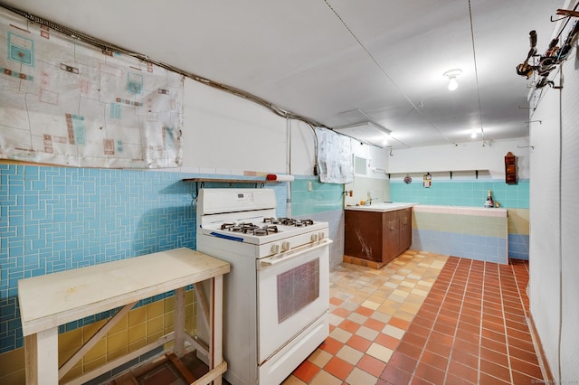 kitchen with white gas stove, light countertops, a sink, and tile walls