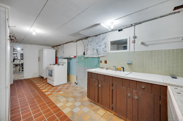 kitchen featuring tasteful backsplash, white range with gas cooktop, brown cabinetry, light countertops, and a sink