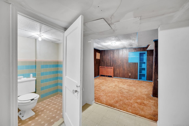 bathroom featuring a paneled ceiling, wood walls, toilet, and tile patterned floors