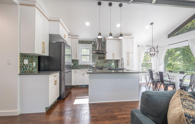 kitchen with a sink, white cabinetry, wall chimney range hood, dark countertops, and pendant lighting