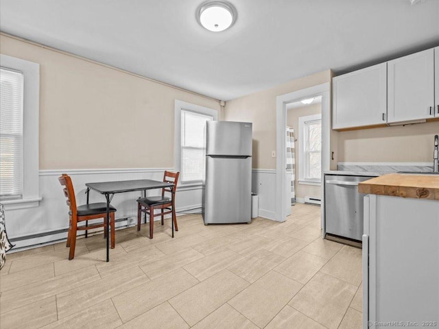 kitchen with a wainscoted wall, appliances with stainless steel finishes, white cabinetry, a baseboard heating unit, and wooden counters