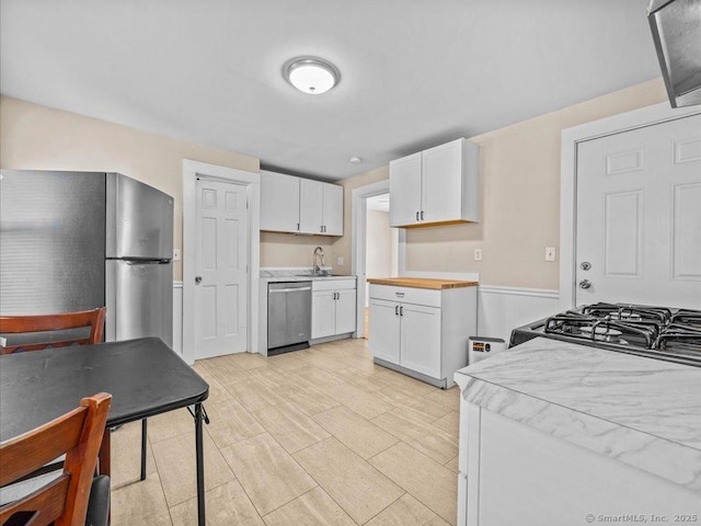 kitchen featuring light wood-style flooring, appliances with stainless steel finishes, light countertops, white cabinetry, and a sink