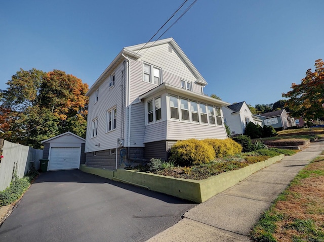 view of front of home featuring a detached garage, fence, aphalt driveway, and an outdoor structure