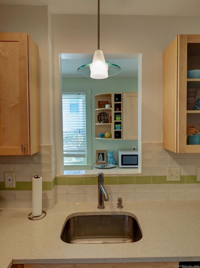 kitchen featuring white microwave, light stone counters, a sink, pendant lighting, and backsplash