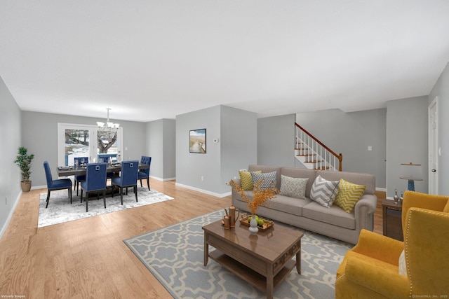 living room featuring light wood-type flooring, baseboards, stairway, and a notable chandelier