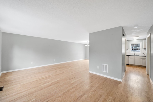 unfurnished living room featuring a notable chandelier, visible vents, light wood-style floors, a textured ceiling, and baseboards