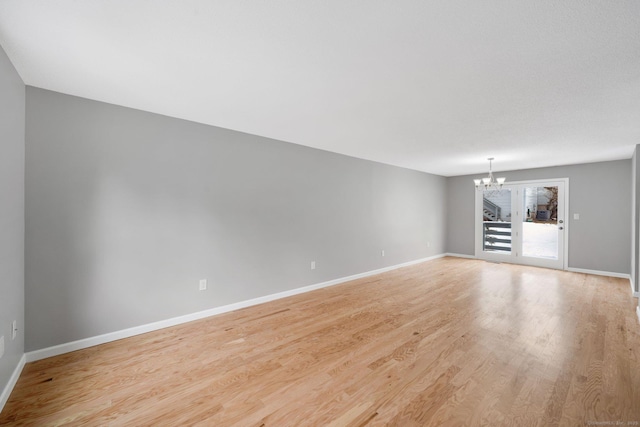 unfurnished living room featuring baseboards, light wood finished floors, and an inviting chandelier