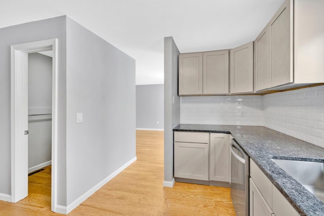 kitchen with light wood finished floors, baseboards, dark stone counters, backsplash, and stainless steel dishwasher