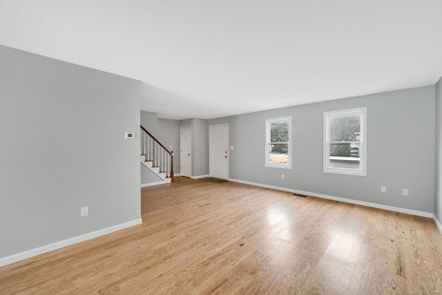 unfurnished living room with light wood-type flooring, baseboards, visible vents, and stairway