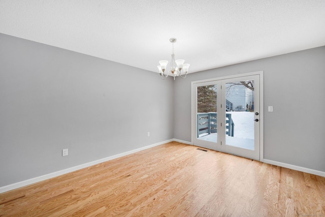 empty room featuring an inviting chandelier, light wood-type flooring, visible vents, and baseboards