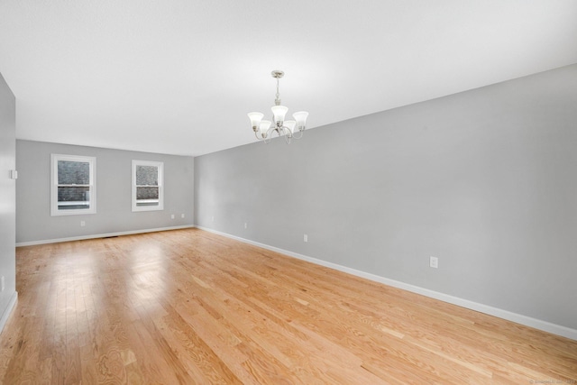 empty room with baseboards, a notable chandelier, and light wood finished floors