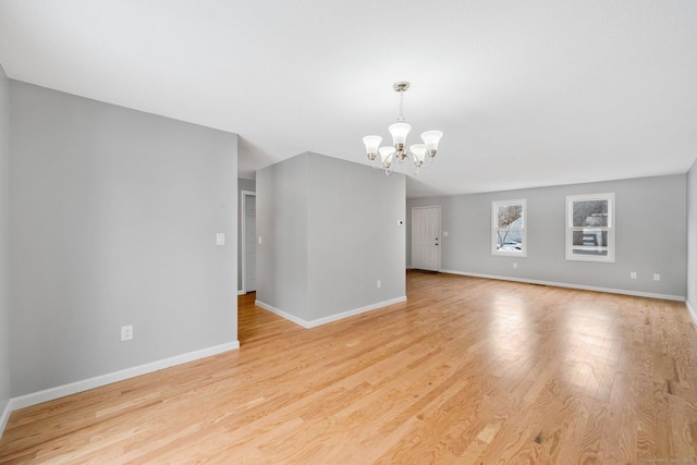 unfurnished living room featuring baseboards, light wood finished floors, and an inviting chandelier