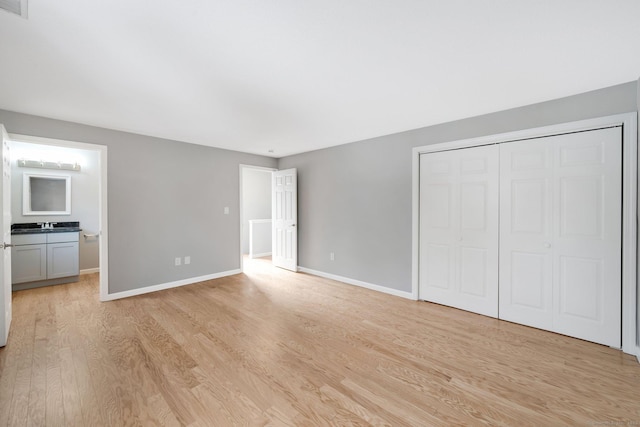 unfurnished bedroom featuring visible vents, baseboards, light wood-style floors, a closet, and ensuite bath