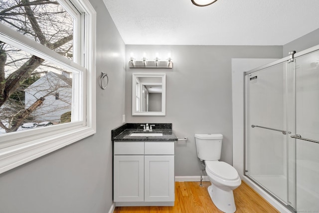 bathroom featuring a stall shower, baseboards, toilet, wood finished floors, and vanity