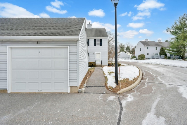 view of front of property featuring aphalt driveway, roof with shingles, a chimney, a garage, and a residential view