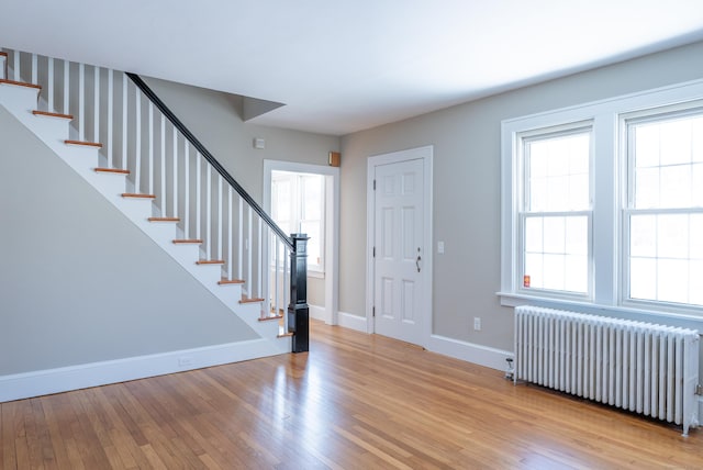 foyer with radiator, a healthy amount of sunlight, stairway, and wood finished floors