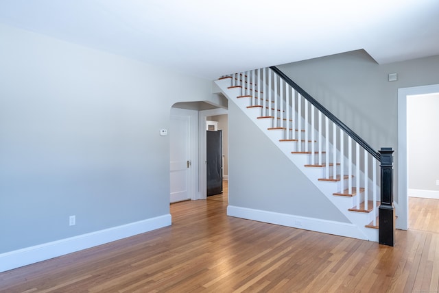 stairway with arched walkways, wood-type flooring, and baseboards