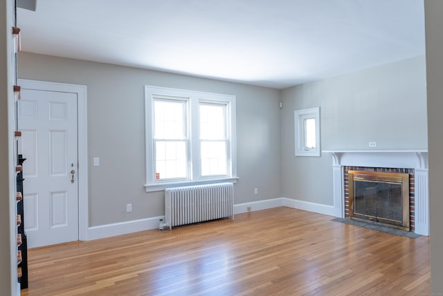 unfurnished living room with light wood-style floors, a brick fireplace, baseboards, and radiator heating unit