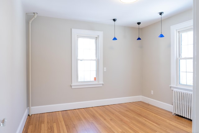 empty room with radiator, plenty of natural light, light wood-style flooring, and baseboards