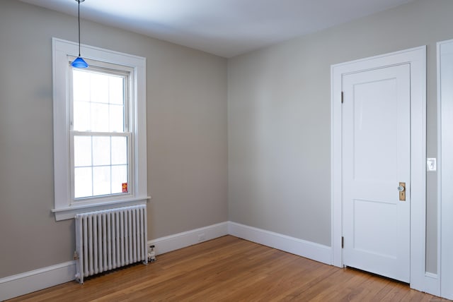 empty room with radiator heating unit, wood finished floors, and baseboards