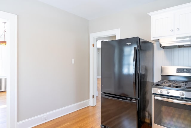 kitchen featuring light wood finished floors, gas stove, freestanding refrigerator, white cabinetry, and under cabinet range hood