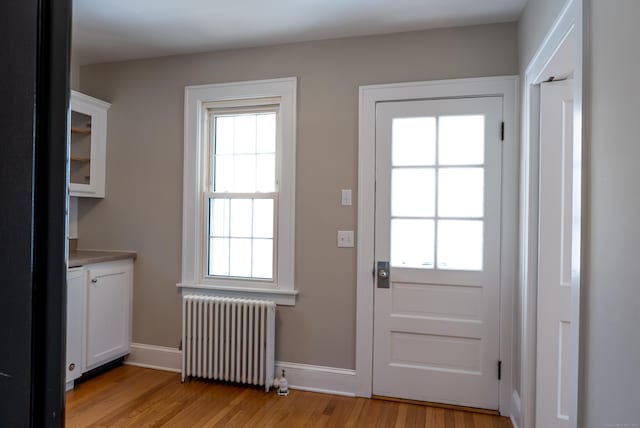 doorway to outside featuring baseboards, light wood finished floors, and radiator