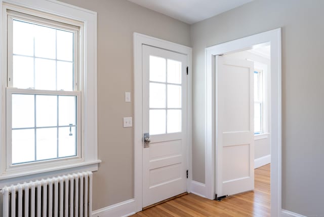 entryway featuring baseboards, a healthy amount of sunlight, light wood finished floors, and radiator heating unit