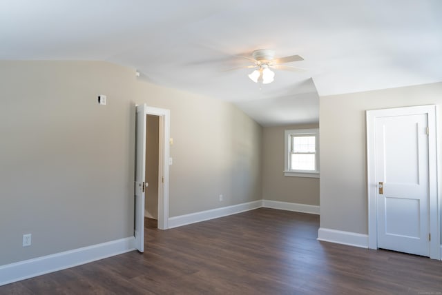 spare room featuring lofted ceiling, dark wood-type flooring, a ceiling fan, and baseboards