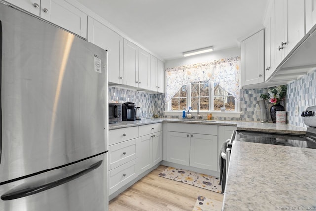 kitchen with decorative backsplash, light wood-style flooring, appliances with stainless steel finishes, white cabinetry, and a sink