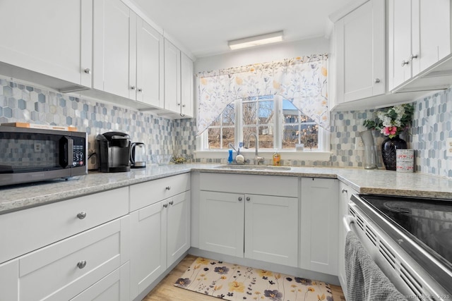 kitchen with tasteful backsplash, light stone counters, stainless steel appliances, white cabinetry, and a sink