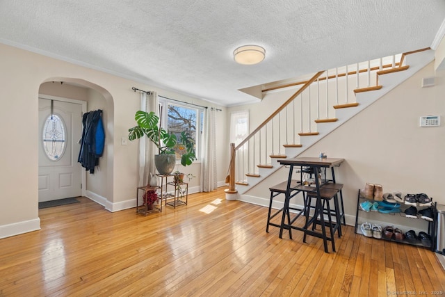 foyer entrance featuring arched walkways, stairway, wood-type flooring, and baseboards