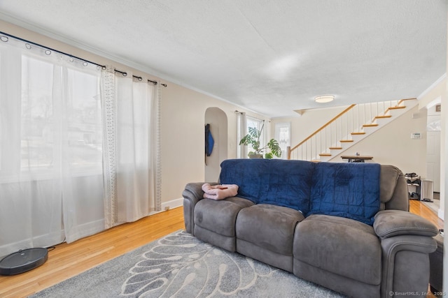 living room featuring arched walkways, crown molding, stairway, a textured ceiling, and wood finished floors