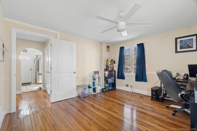 office space featuring arched walkways, ceiling fan, visible vents, baseboards, and wood-type flooring