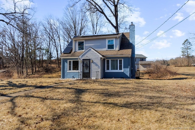 view of front of property featuring a shingled roof, a chimney, and a front lawn