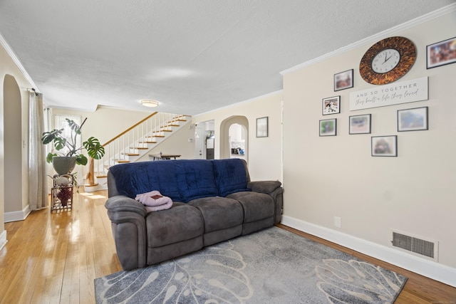 living room with arched walkways, visible vents, stairway, light wood-type flooring, and crown molding