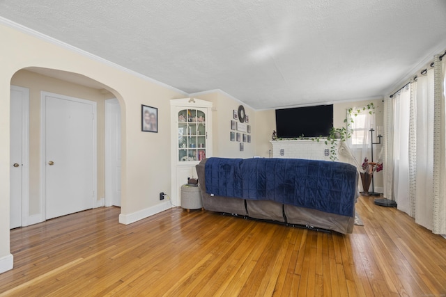 living area with light wood-style floors, arched walkways, ornamental molding, and a textured ceiling