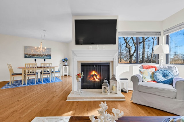 living room featuring a warm lit fireplace, a chandelier, wood finished floors, and baseboards